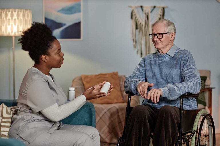 A resident receives medication assistance from a caregiver in a bright, home-like common area.